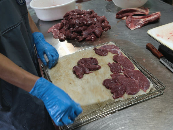 薄く切った鹿肉を、重ならないように一枚ずつ網に並べる手元